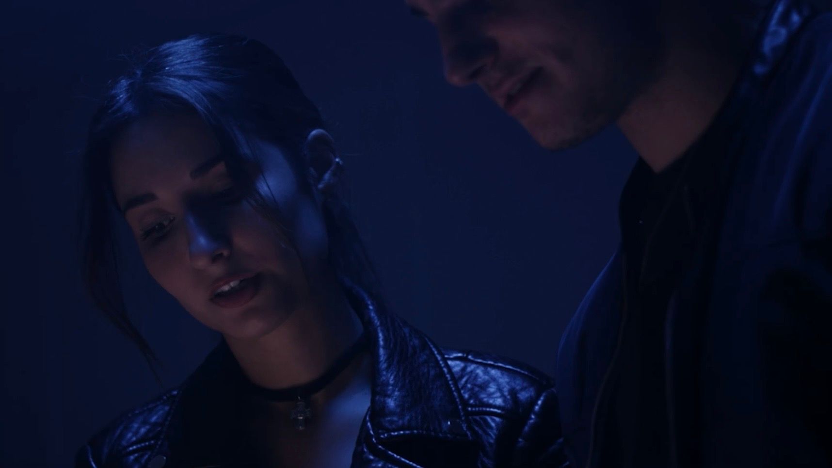 Jessica Curado in character beside another actor, in a scene lit in deep blue.